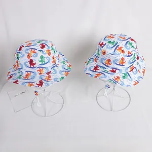 Detail showing two white cotton kids sun hats with colorful dinosaur cartoon prints and chin straps