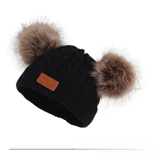 Détail du bonnet en tricot noir avec pompons en fourrure marron et écusson en cuir