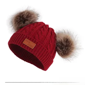 Détail du bonnet rouge en maille torsadée pour enfant avec pompons en fausse fourrure
