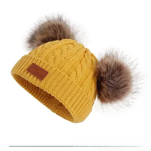 Détail du bonnet tricoté jaune pour enfant avec pompons en fourrure et écusson cuir