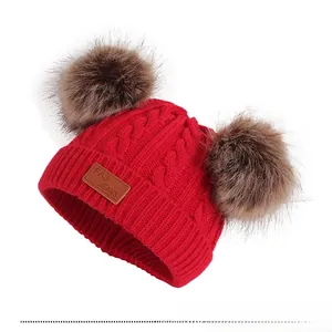 Détail du bonnet rouge en maille torsadée pour enfant avec deux grands pompons en fausse fourrure