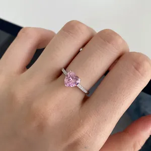 Close-up of heart-shaped pink gemstone ring with micro-paved silver band on finger
