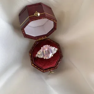 Macro view of emerald cut pink gemstone ring with side stones in a red velvet gift box