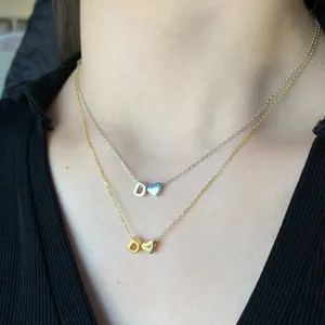 Macro detail of gold and silver layered necklace featuring D-letter and heart pendants