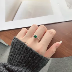 Close-up of S925 sterling silver ring with green zircon on model hand against desk