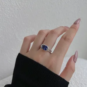 Nahaufnahme des rechteckigen blauen Zirkonia-Rings mit Diamant-Halo am Finger