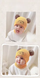Detail of yellow knit baby hat with bear embroidery and double faux fur pom-poms