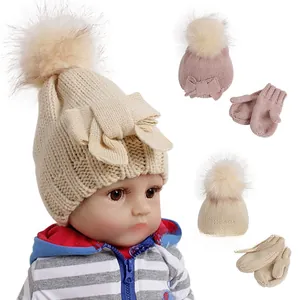 Detail of baby knitted hat and mittens set with fuzzy pom-poms and bow in beige and pink