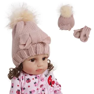 Detail of pink knitted baby hat with plush pompom and matching mittens set
