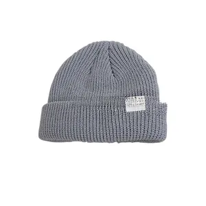 Detailed view of gray knit beanie featuring white woven smiley face patch for kids