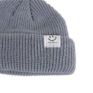 Close-up of grey ribbed knit beanie featuring a white woven patch with a black smiley face