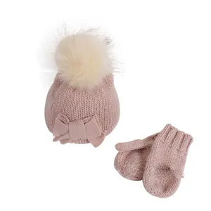 Detail of pink baby knit hat with large faux fur pom-pom and matching mittens set