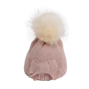 Detailed knit texture of pink baby winter hat with large faux fur pompom and bow