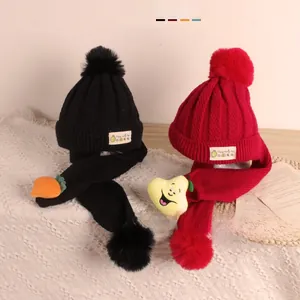 Détail d'un ensemble bonnet et écharpe tricotés pour bébé avec pompons et fruits 3D