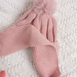 Détail d'un ensemble bonnet et écharpe en maille torsadée rose avec pompons pour enfants