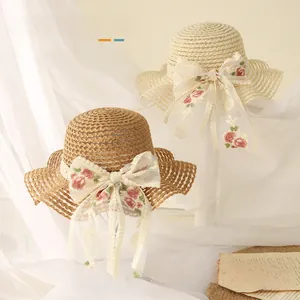 Détail de chapeaux en paille pour enfants avec nœuds en dentelle et broderie rose