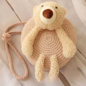 Vue détaillée d'un sac rond en paille tressée pour enfants avec un petit ours en peluche