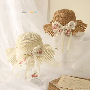 Détail de chapeaux de paille bébé avec nœuds en dentelle blanche et broderie fleurie
