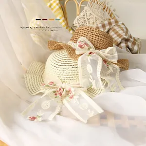 Détail de chapeaux de paille pour bébé avec nœuds en dentelle brodée blanc et caramel
