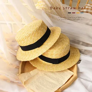 Kids summer straw hat with black ribbon on a wooden tray for sun protection