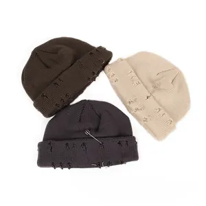 Close-up of distressed knit beanies with metal pins and rings in brown, beige, and gray