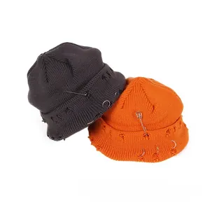 Detail of distressed knitted beanie hats with metal safety pins and ring accessories