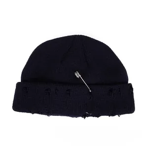 Detail of distressed knitted beanie with metal rings and decorative safety pin decoration