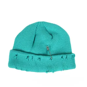 Detail of teal knit beanie featuring metal safety pin, three rings, and distressed holes