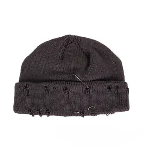 Detail of dark grey knit beanie with silver safety pins, rings, and distressed torn edges