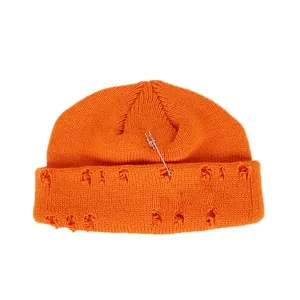 Detail of orange knitted beanie with distressed holes, safety pin and metal rings