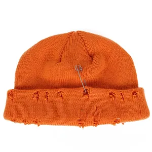 Detail of distressed orange knit beanie with metal pin and triple silver ring accents
