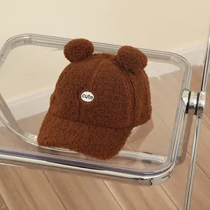 Brown fleece kids baseball cap with cute bear ears and embroidered patch on a modern chair