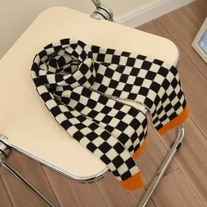 Black and white checkerboard knit scarf for kids with orange edges on a chair