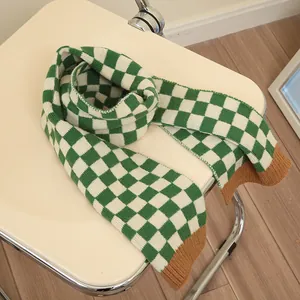 Green and white checkerboard knit scarf for kids with brown ribbed trim on a chair
