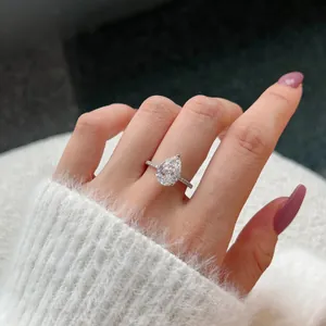 Close-up of a pear-cut silver ring with halo stones on a model's hand with soft background