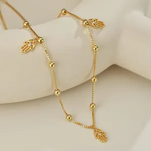 Collier chaîne box dorée avec pendentifs main de Hamsa et zircons sur support beige
