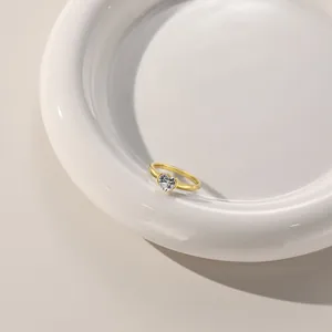 Macro shot of minimalist gold plated heart zircon ring on white ceramic tray