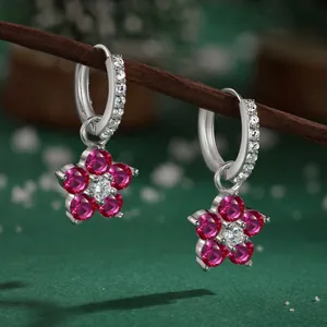 Macro shot of silver flower drop earrings with pink zircons on a dark branch