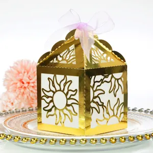 Close-up of golden laser-cut gift box with sun pattern and pink ribbon on a dinner plate