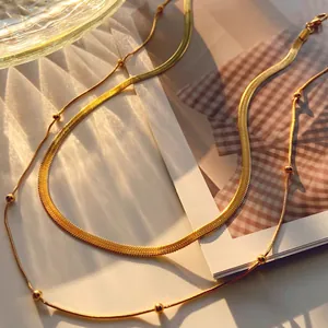 Detail of layered gold snake chain and beaded necklace with polished metallic texture