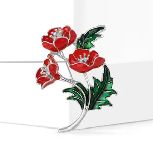 Detalle de broche de amapola roja con bordes plateados y hojas de esmalte verde