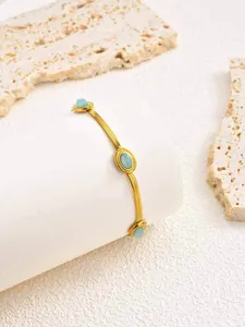 Dettaglio del bracciale a catena a serpente dorata con tre pietre turchesi su supporto in pietra