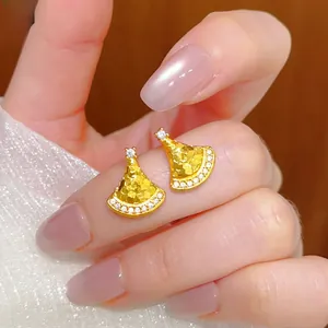 Close-up of golden fan-shaped earrings with honeycomb texture and sparkling crystals