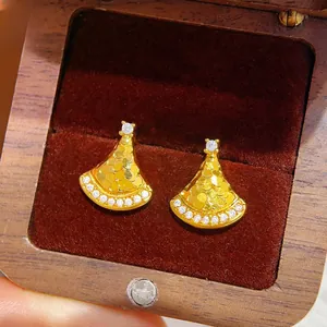 Macro shot of gold fan-shaped stud earrings with embedded crystals in a jewelry box