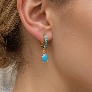 Primo piano di eleganti orecchini a goccia in oro con turchese indossati da modella
