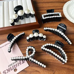 Elegant black hair claws with white pearl accents in various geometric designs on a tray