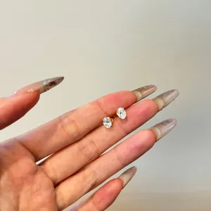 Macro shot of oval-cut crystal earrings with 4-prong gold setting held on a finger