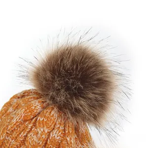 Close-up of bright orange cable knit beanie with fluffy faux fur pompom detail