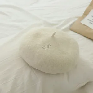 Close-up of cream wool felt beret with stem detail on a minimalist soft fabric background