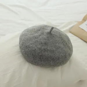 Detailed close-up of grey wool beret hat for girls on white textured fabric backdrop